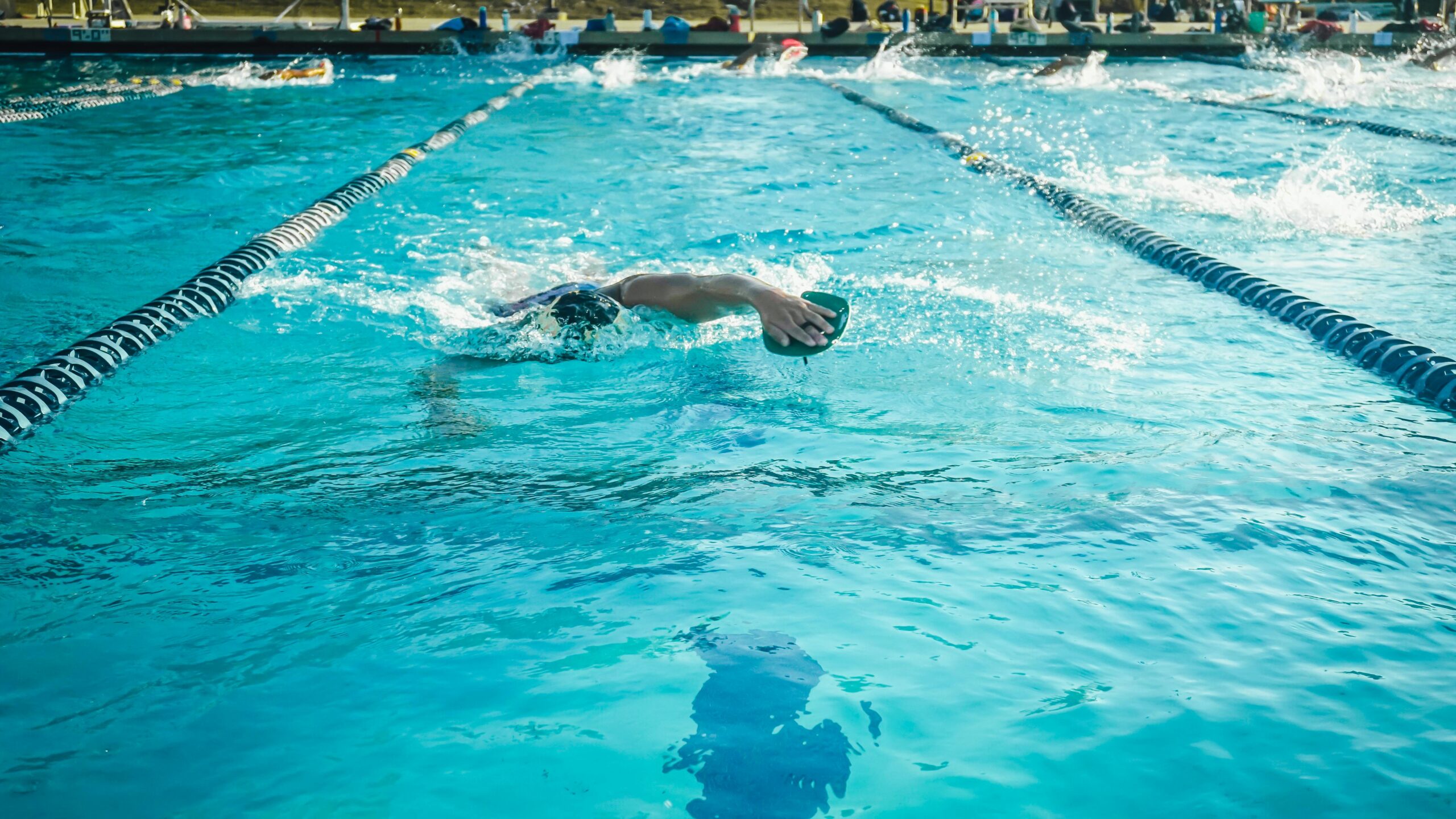 An adult swimmer practicing freestyle in an outdoor Olympic-size pool.